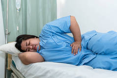 亚洲肥胖妇女病人躺在病人床上，腹部疼痛严重，从胃炎、肠炎到人和医疗保健观念.