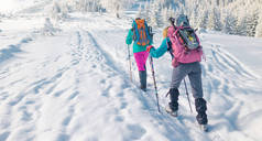 两名妇女背着雪鞋走路，冬天徒步旅行，两名男子冬天在山上徒步旅行，带着登山装备