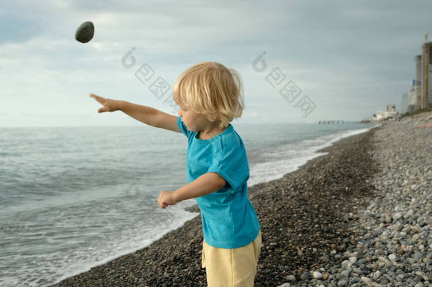 一个小男孩在海滨<strong>玩耍</strong>，他把石头扔进了水里。<strong>海边</strong>的家庭度假。高质量的4k镜头