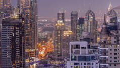 迪拜的滨海区和媒体城，拥有现代化的摩天大楼和办公楼，从天到夜的过渡时间已经过去了。背景下绿化公园附近的立交桥和交叉路口的交通情况