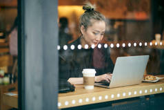 用手提电脑拍摄的在咖啡店工作的亚洲中年女商人的玻璃照片