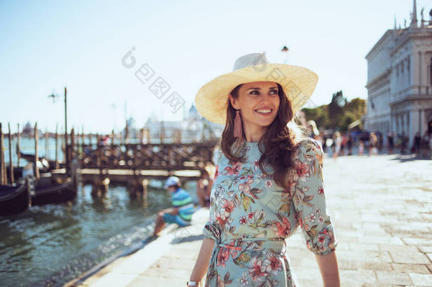 happy modern woman in floral dress with hat having walking tour on embankment in Venice, Italy.