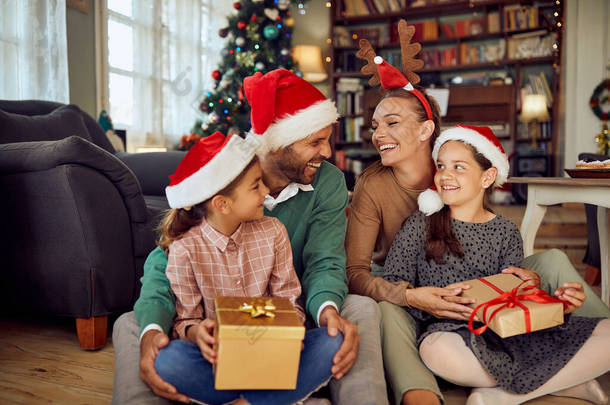 Happy little girls holding presents and having fun with their parents on Christmas day at home.