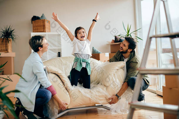 Happy family having fun at their new home. Focus is on little girl with raised arms.