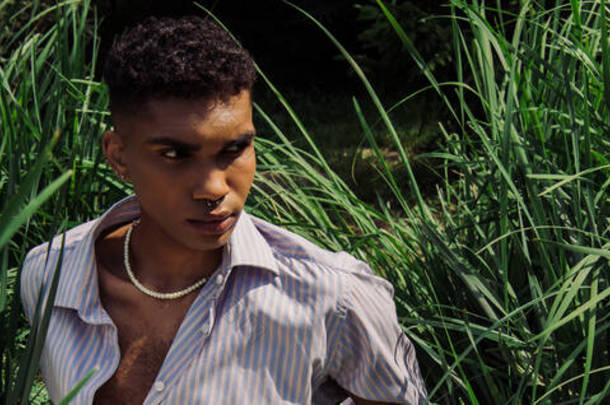 stylish african american man looking away while sitting on green grass, <strong>banner</strong>