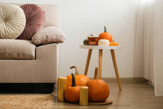 Bunch of pumpkins of different kinds, shapes and colors on the floor and a table near the couch of a