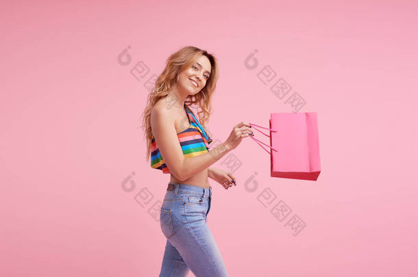销售理念。肖像一个兴奋的美丽年轻女子穿着五颜六色的夏季衣服拿着购物袋隔离在粉红色背景。在包上签名或文本的空间