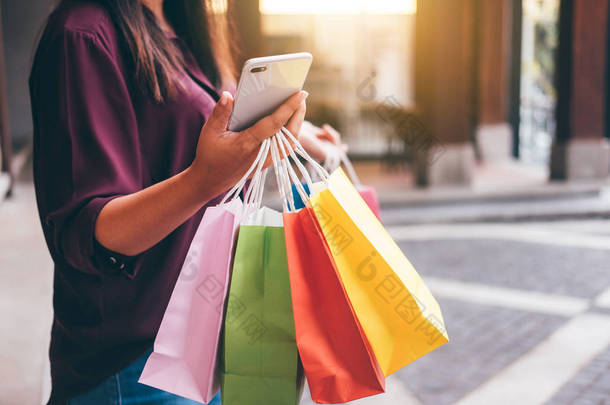 消费主义, 购物, 生活方式观念, 年轻女子手持五颜六色的购物袋和智能手机享受购物.