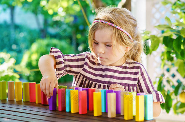 Little preschool girl playing board game with colorful bricks domino. Happy child build tower of woo