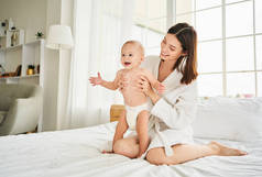 年轻的白人母亲穿着尿布在卧室的床上和她刚出生的儿子玩耍。淋浴后的概念、婴儿护理、母性.