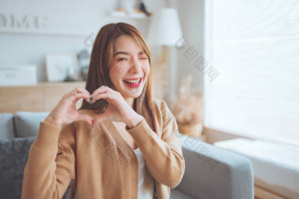 Close up of happy young asian woman smiling and showing hands sign heart shape looking at camera. He