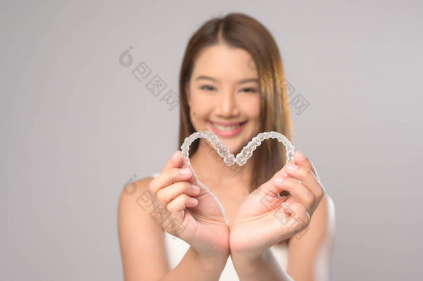 一名年轻的微笑女性，在白色背景工作室、牙齿保健和牙齿矫正的概念下，手持<strong>无创</strong>矫形器架.