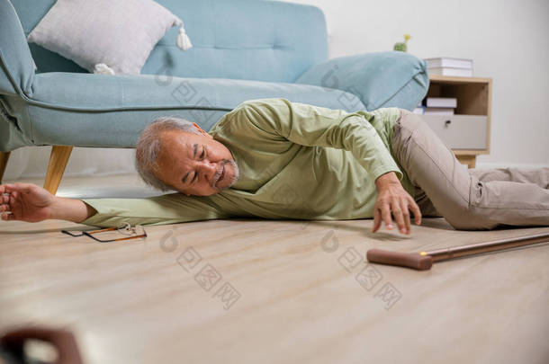 亚洲老人倒在地板上，用木棍走路；生病的老人躺在沙发旁边，躺在客厅里；老年人单独做理疗后出了车祸