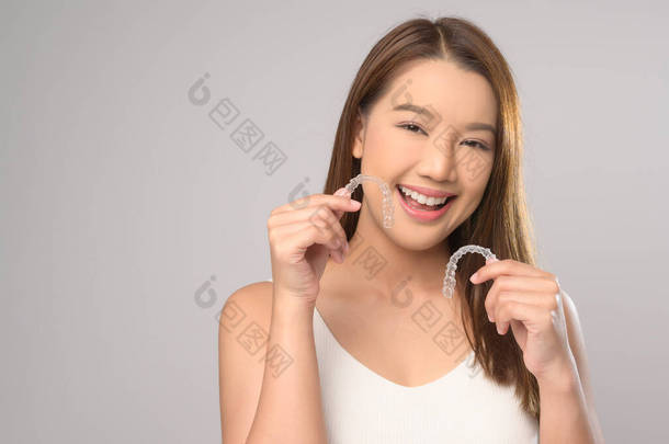 一名年轻的微笑女性，在白色背景工作室、<strong>牙齿</strong>保健和<strong>牙齿矫正</strong>的概念下，手持无创矫形器架.