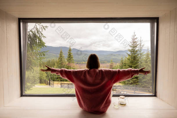 女人坐在窗台上沉思，欣赏高山上的全景。娱乐和<strong>逃避</strong>现实的概念