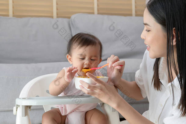 一位年轻的母亲帮助婴儿在婴儿椅上吃混合食品