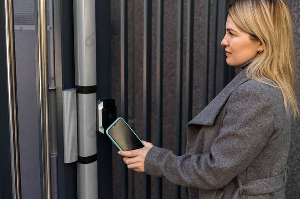 女人用智能手机把<strong>门锁</strong>锁在门上。使用可无钥匙接达的智能<strong>电子</strong>锁的概念.