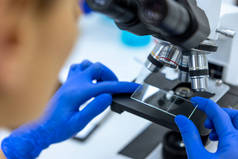 穿着蓝色手术手套在实验室工作的难以辨认的科学家，医生使用显微镜分析幻灯片