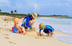 父亲和两个孩子在夏天的海滩上玩沙子