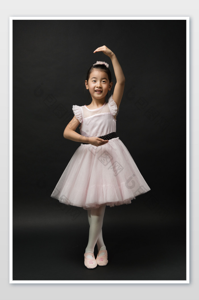 黑色背景穿着粉色纱裙摆芭蕾姿势的小女孩