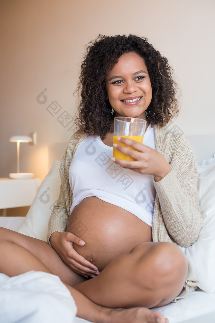 黑人孕妇坐在床上端着橙汁