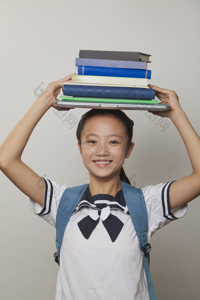 学生小女孩校服背着书包头顶着书本学习微笑
