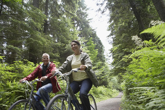 绿色调林中骑行的夫妻摄影图