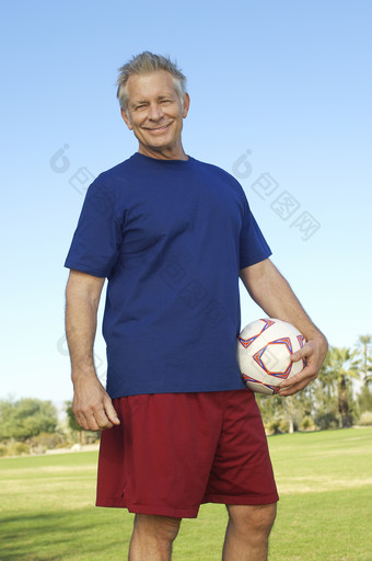老人抱着足球站在草坪