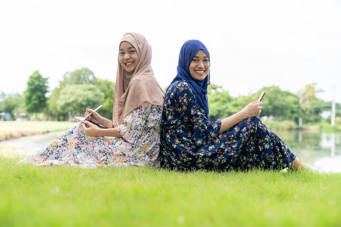 草坪上背对背坐着的穆斯林女孩