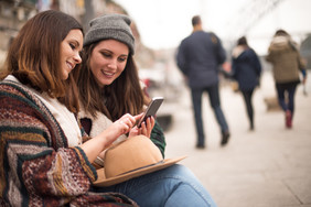 两个年轻女孩坐在街头看手机