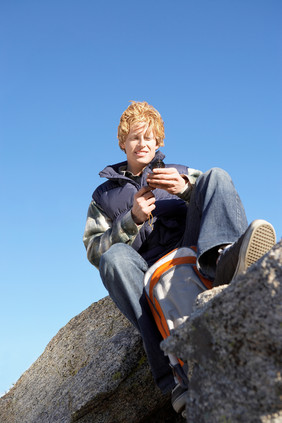 坐石头上玩手机的男孩