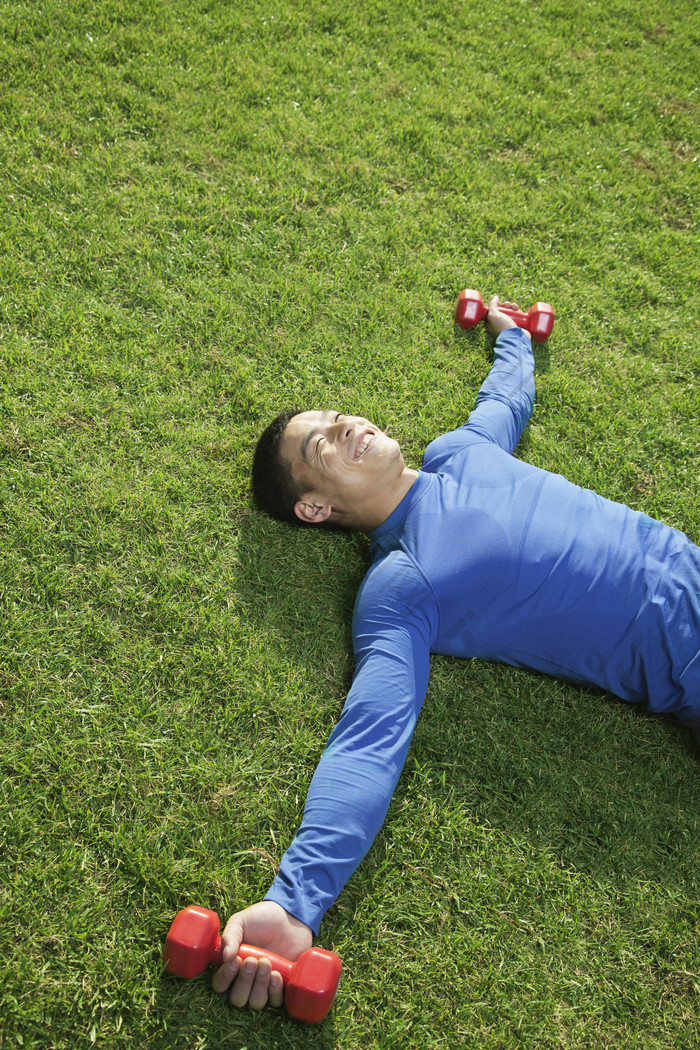 躺在草地上的年轻男子举着哑铃摄影照