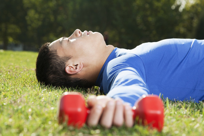 躺在草地上的年轻男子举着哑铃摄影