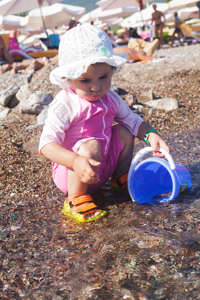 儿童蹲在海滩拿水桶舀水