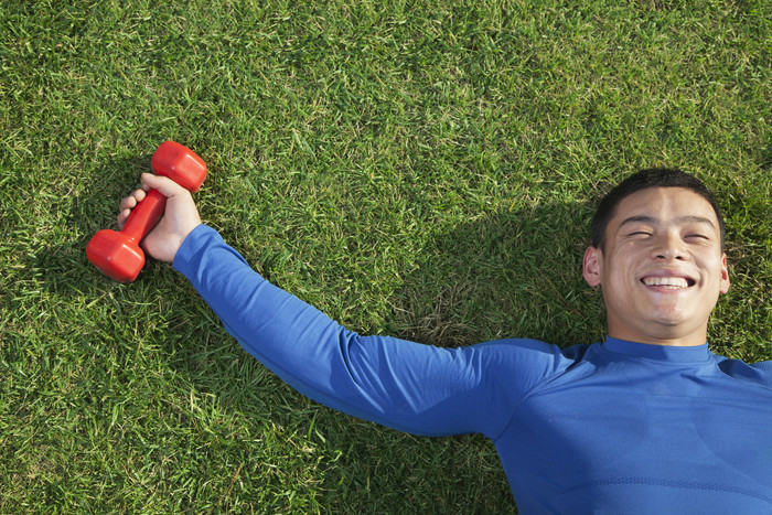 躺在草地上的年轻男子举着哑铃摄影图