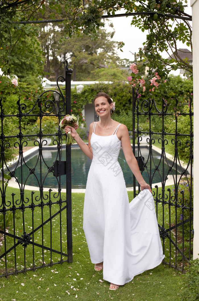 新娘提着裙摆站在铁门前