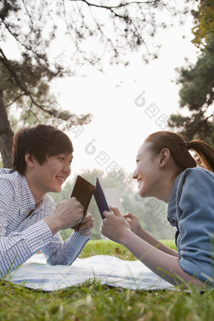 草地上情侣学生读书趴着对视微笑幸福阳光