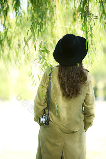 戴着帽子在柳树下看风景的美女背影图片