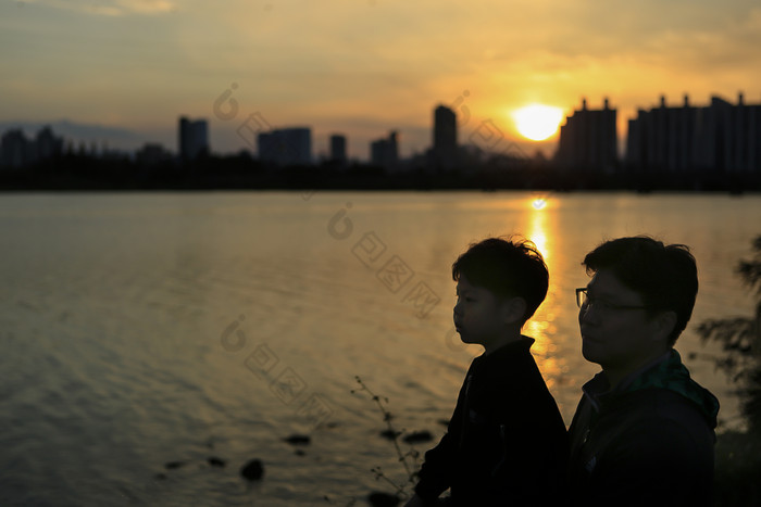 夕阳下坐在湖边的两父子
