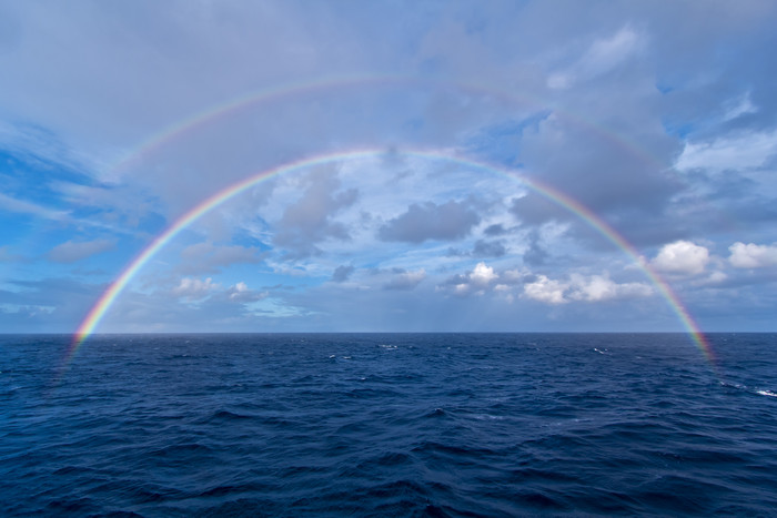 蓝色天空下出现在海上的两轮彩虹