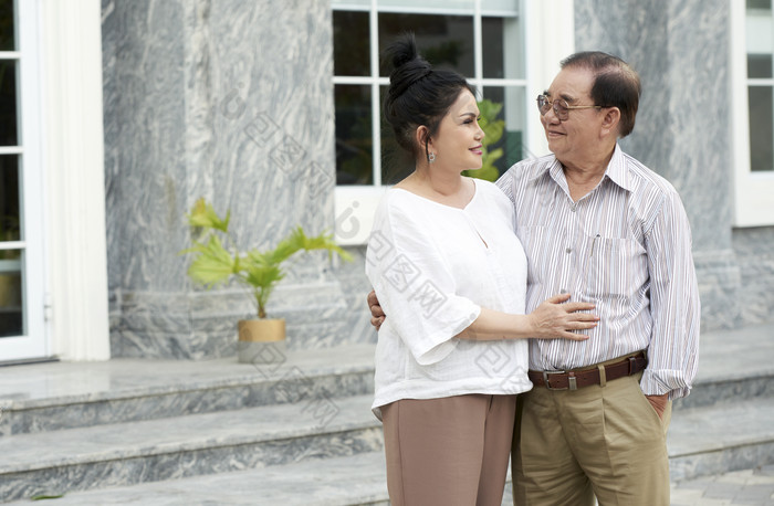 在房子前面拥抱的老年夫妻
