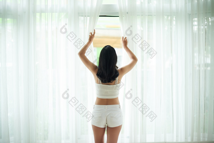 卧室拉窗帘的女人摄影图