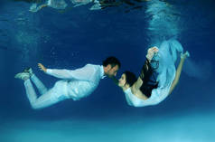 新娘和新郎穿着白色婚纱在水池里游泳。水下婚礼