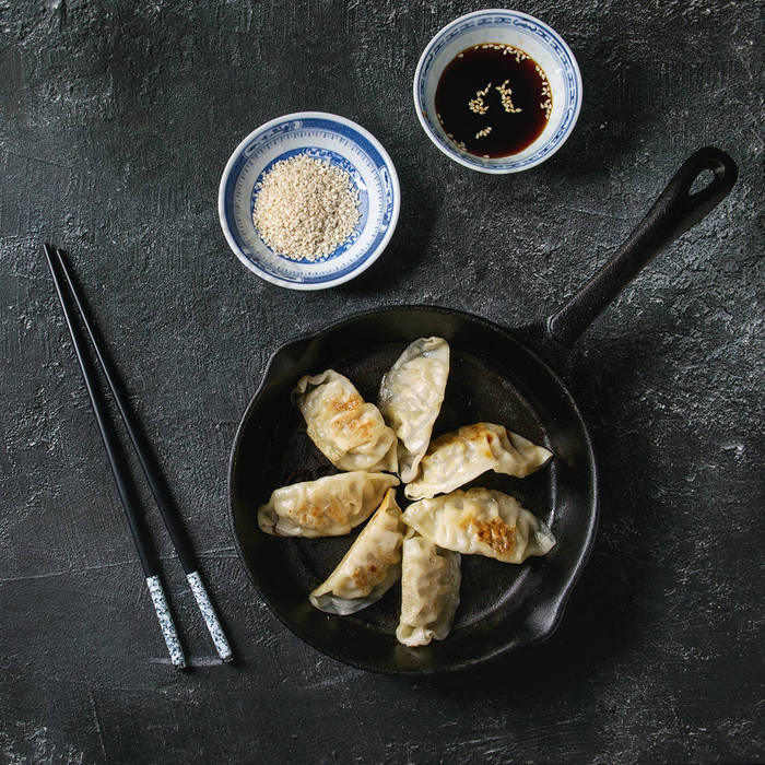 亚洲饺子 Gyozas 锅贴炒在铸铁锅上, 配有筷子和一碗酱油, 上面有黑色的纹理背景。顶部视图, 空间.