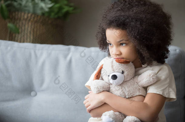 不安的孤独的非洲女孩抱着泰迪熊看着离开