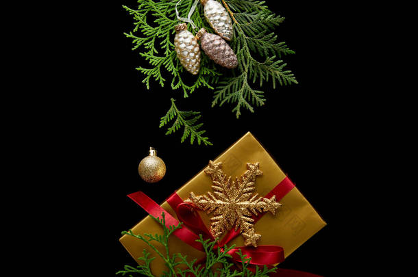 金光闪闪的圣诞装饰、绿色的thuja枝条和装在黑色上的礼品盒的顶视图