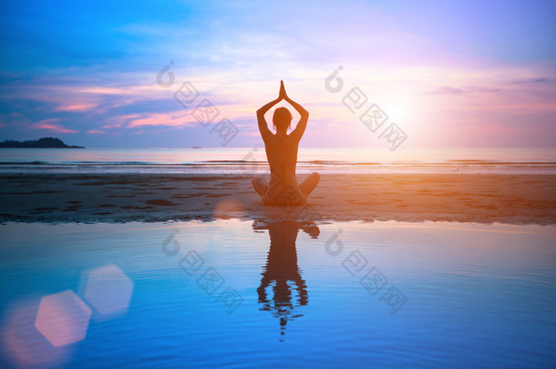 剪影年轻女子在日落时<strong>练瑜伽</strong>在海滩上