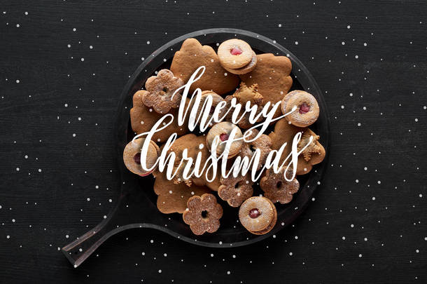 圣诞饼干放在黑色木制桌子上的平底锅上，上面印有圣诞快乐和降雪的图解