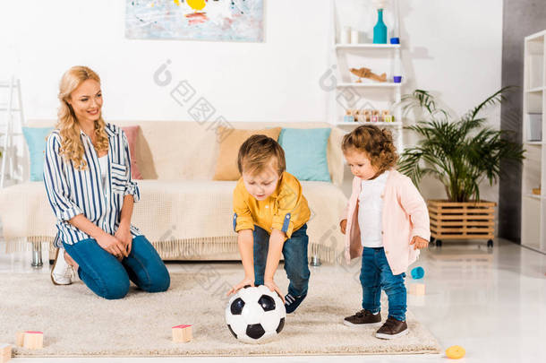微笑的母亲看着可爱的小孩子在家里玩足球球