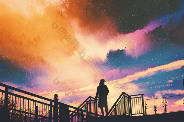 男子站在反对色彩斑斓的天空的行人天桥